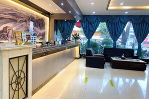 Een hotellobby met een receptiebalie, een zithoek en grote ramen.