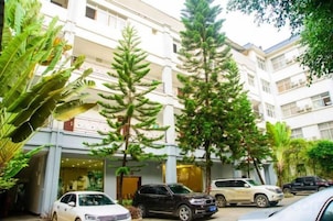 Un edificio de varios pisos con un patio, coches aparcados y árboles altos.