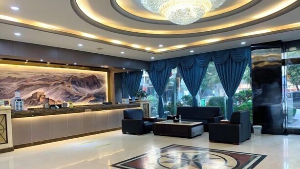 A modern lobby with a reception desk, seating area, and a large mural. - Xinhe Business Hotel (Yingjiang)