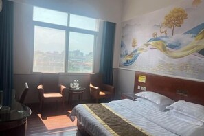Hotelkamer met een bed, twee stoelen, een kleine tafel met waterflessen, een raam met uitzicht op de stad en een muurschildering.