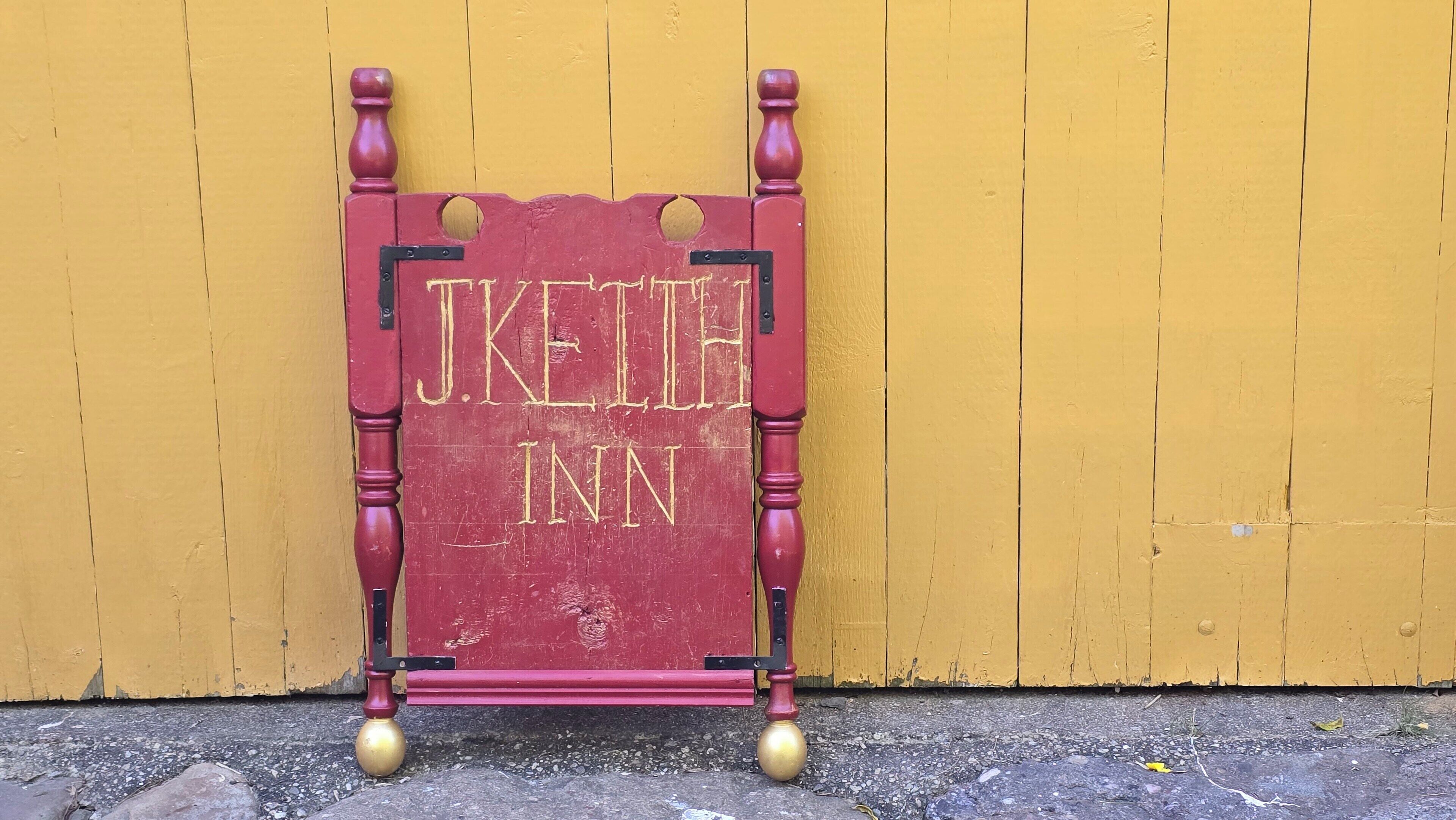 A red sign with gold lettering reading "J. Keith Inn" against a yellow wall.