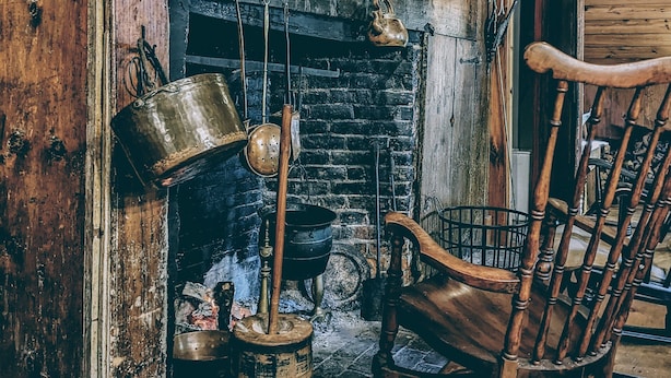 Een rustiek interieur met een houten open haard, een schommelstoel en diverse keukengerei.