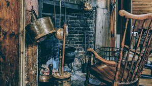 A rustic interior with a wooden fireplace, a rocking chair, and various cooking utensils. - Josiah Keith House (Easton)