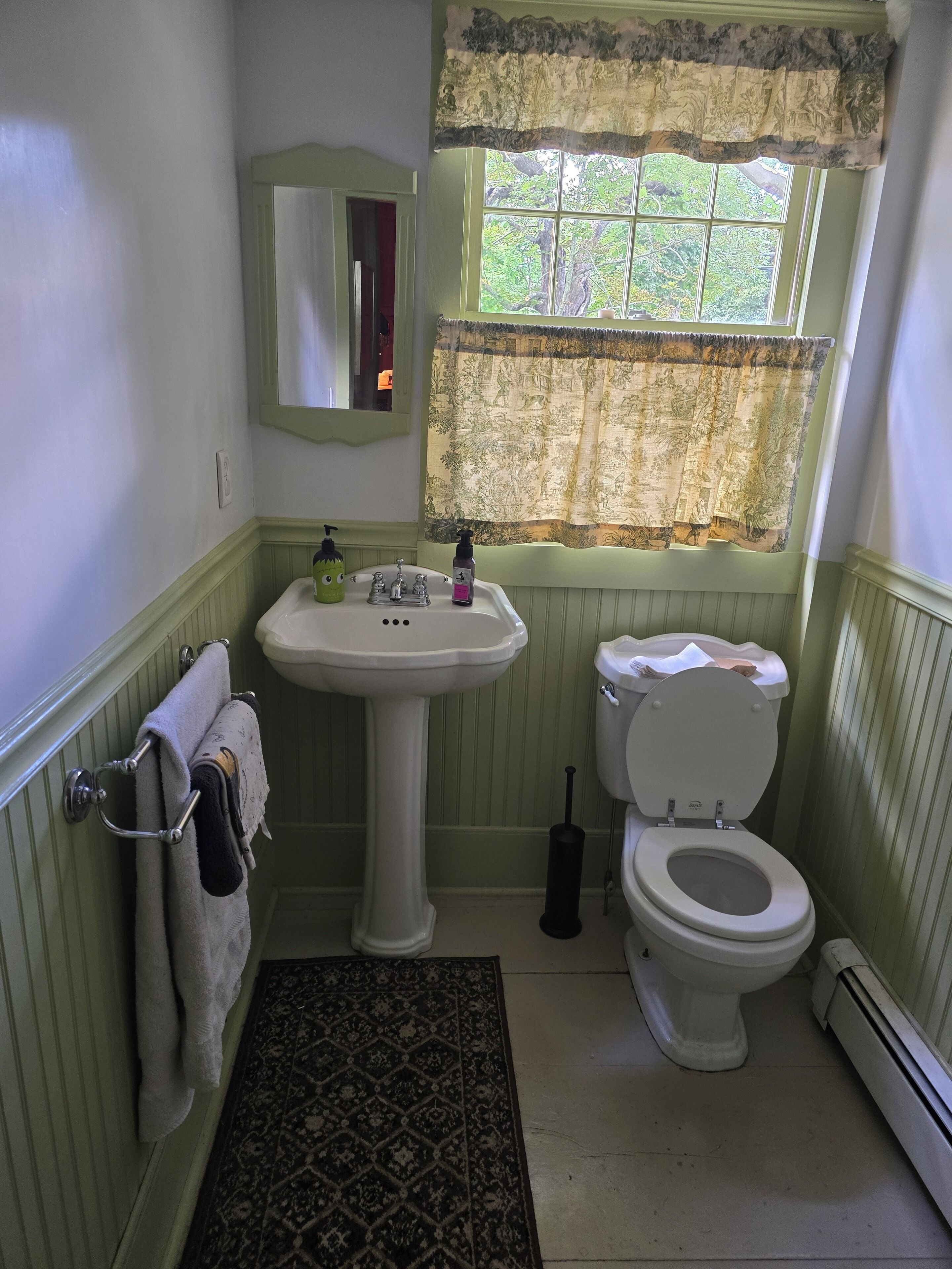 Baño con lavamanos pedestal, inodoro y ventana con cortina floral.