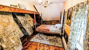 Een kleine kamer met een bed, een houten trap, een kroonluchter en gordijnen met een patroon.