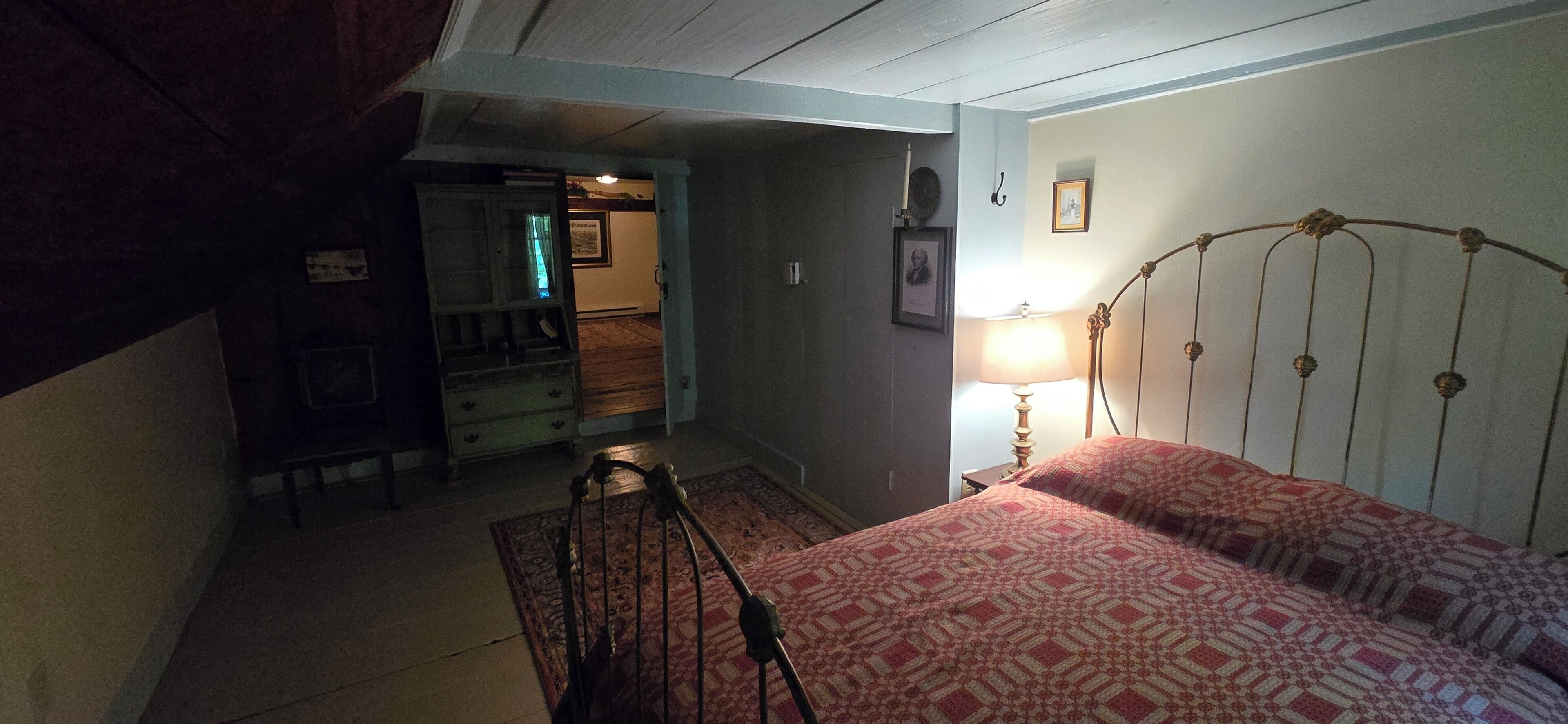 A bedroom with a bed, a dresser, a lamp, and a door leading to another room.