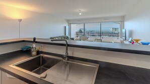 Une cuisine moderne dotée d’un évier en acier inoxydable, d’une fenêtre donnant sur le paysage urbain et d’un balcon offrant une vue sur les bâtiments et un pont.