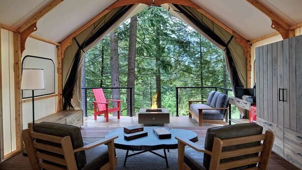 Une pièce aménagée comme une tente, avec une cheminée, des sièges et une vue sur la forêt.