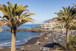 Una playa con palmeras, sillas de sol y un edificio al fondo.