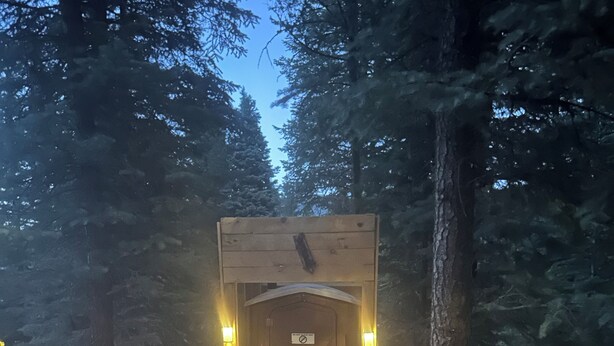 A wooden structure with a sign, surrounded by trees and rocks, with lights on either side.