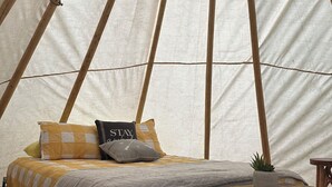 A cozy interior of a tent with a bed, pillows, a small table, and a wooden chest.
