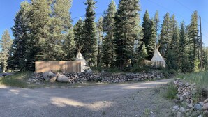 A gravel path leading to a wooden fence and two tipi-style structures in a forested area.
