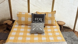 A bed with a yellow and white checkered bedspread, a grey pillow with directional arrows, and a black pillow with "STAY awhile" text.