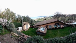 A house with a sloped roof, a small attached structure, and a patio area with a table and chairs. - Breathtaking view of the lake and castle surrounded by holm oaks and oaks (Lazio)