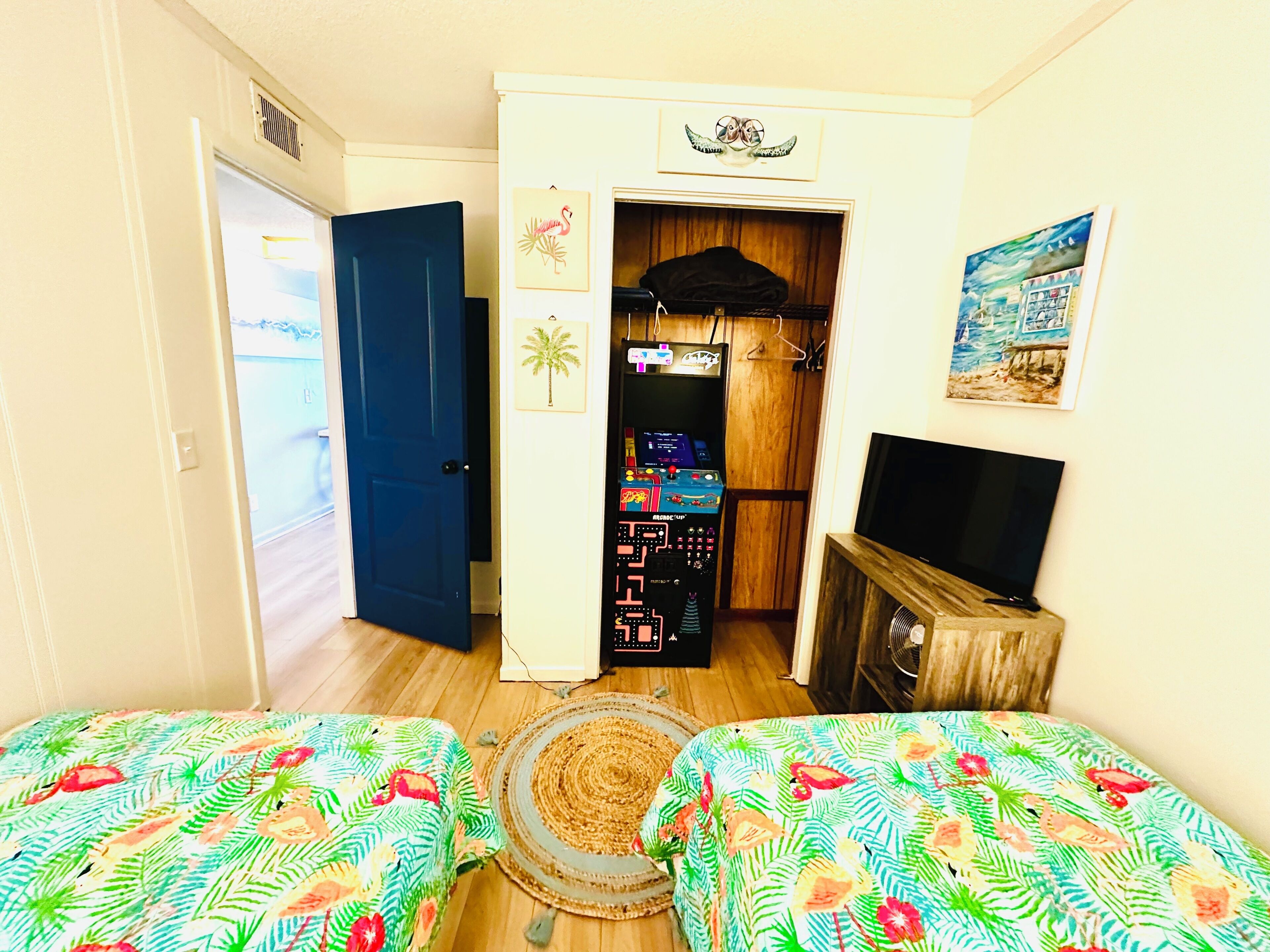 A room with two beds, a TV, a gaming console, and a door leading to another room.