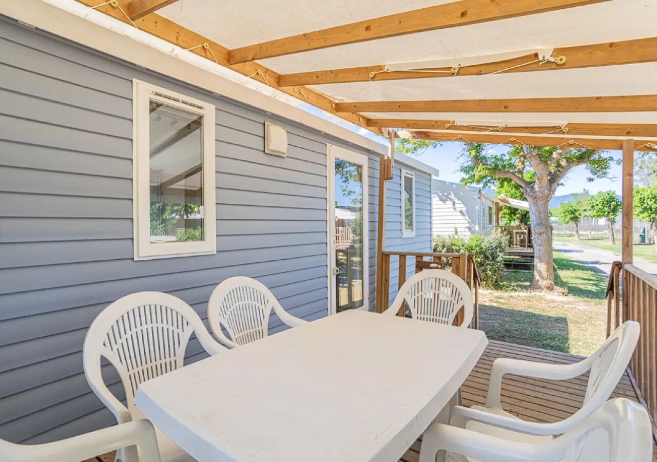A covered patio with a table and chairs, a wooden pergola, and a view of a backyard with a tree.