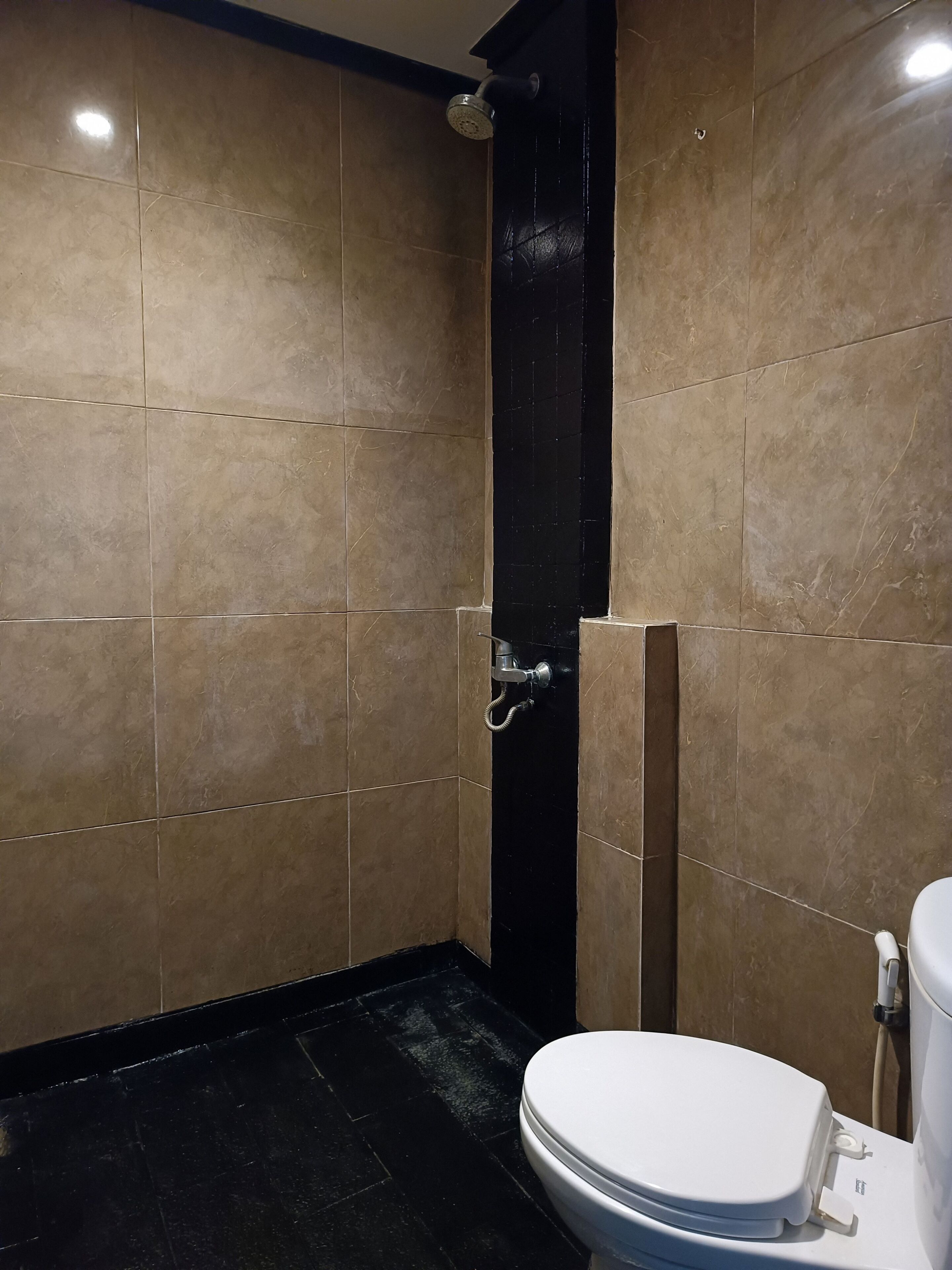A bathroom with beige tiles, a black shower enclosure, and a white toilet.