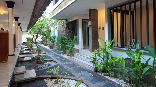 Un couloir d’hôtel moderne avec un sol carrelé, des plantes en pot et un chemin en pierre.