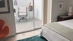 Ein Schlafzimmer mit einem Bett, einem grünen Teppich, einem Sessel und Blick auf einen Balkon mit einem Stuhl und Pflanzen.