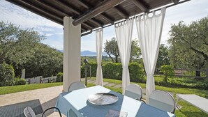 Une terrasse extérieure avec une table et des chaises, une pergola au-dessus et une vue sur la verdure et les montagnes lointaines.