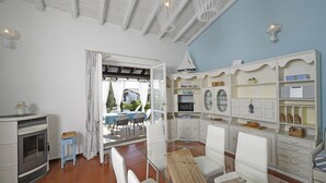 Une pièce avec une cheminée, des meubles blancs, un coin cuisine et une vue sur une terrasse extérieure.