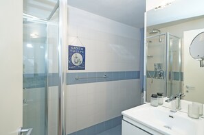 Un baño moderno con cabina de ducha de vidrio, un lavabo blanco con espejo y pared revestida de azulejos azules y blancos.