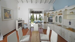 Une pièce spacieuse comprenant un coin repas, des meubles blancs, une cheminée et une vue sur l’extérieur, visible à travers une porte vitrée.