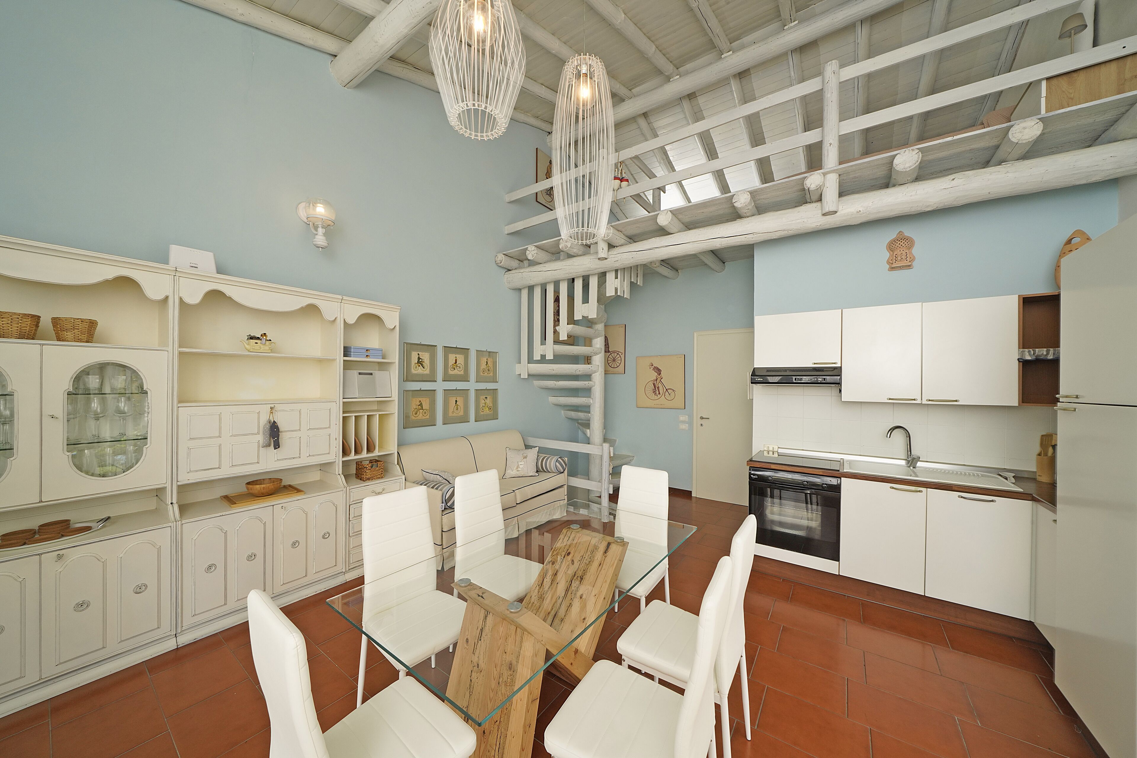 A modern kitchen with white cabinetry, a dining area with a glass table, and a spiral staircase.