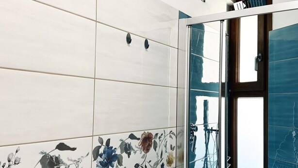 A bathroom with white tiles and floral patterns, a glass shower door, and a view of power lines outside. - M406 - Marcelli, new studio apartment facing the sea (Marcelli)