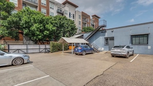 A parking area with two cars, a staircase leading to a building, and a fenced area with trees.