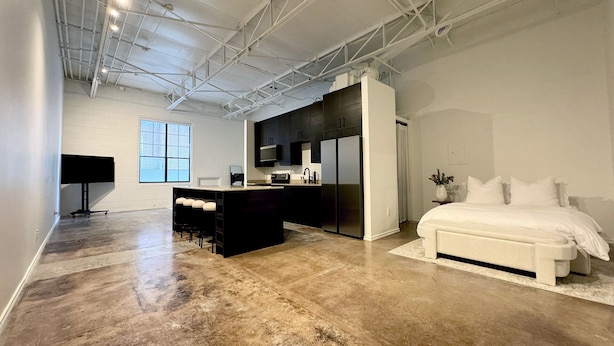 A modern, spacious room with a large bed, a kitchen area, and a seating area with a bar.