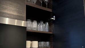 A kitchen with a built-in wine rack holding various glassware, a stainless steel range hood, and a modern faucet.