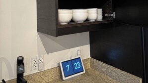 A kitchen with a dark wooden cabinet containing white and pink bowls, a digital clock displaying 7:23, and a black faucet.