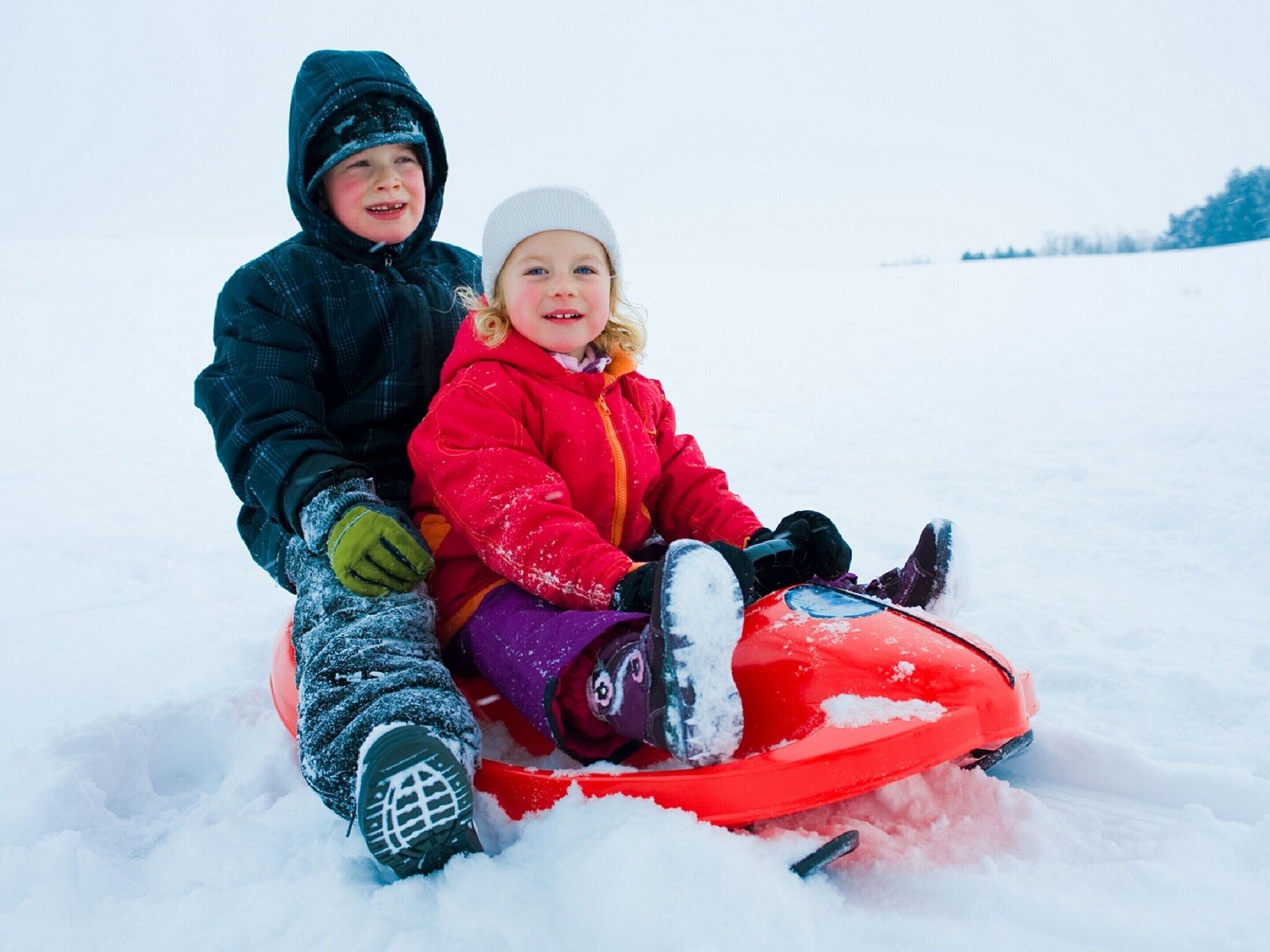 Two children sitting on a red sled in a snowy landscape.