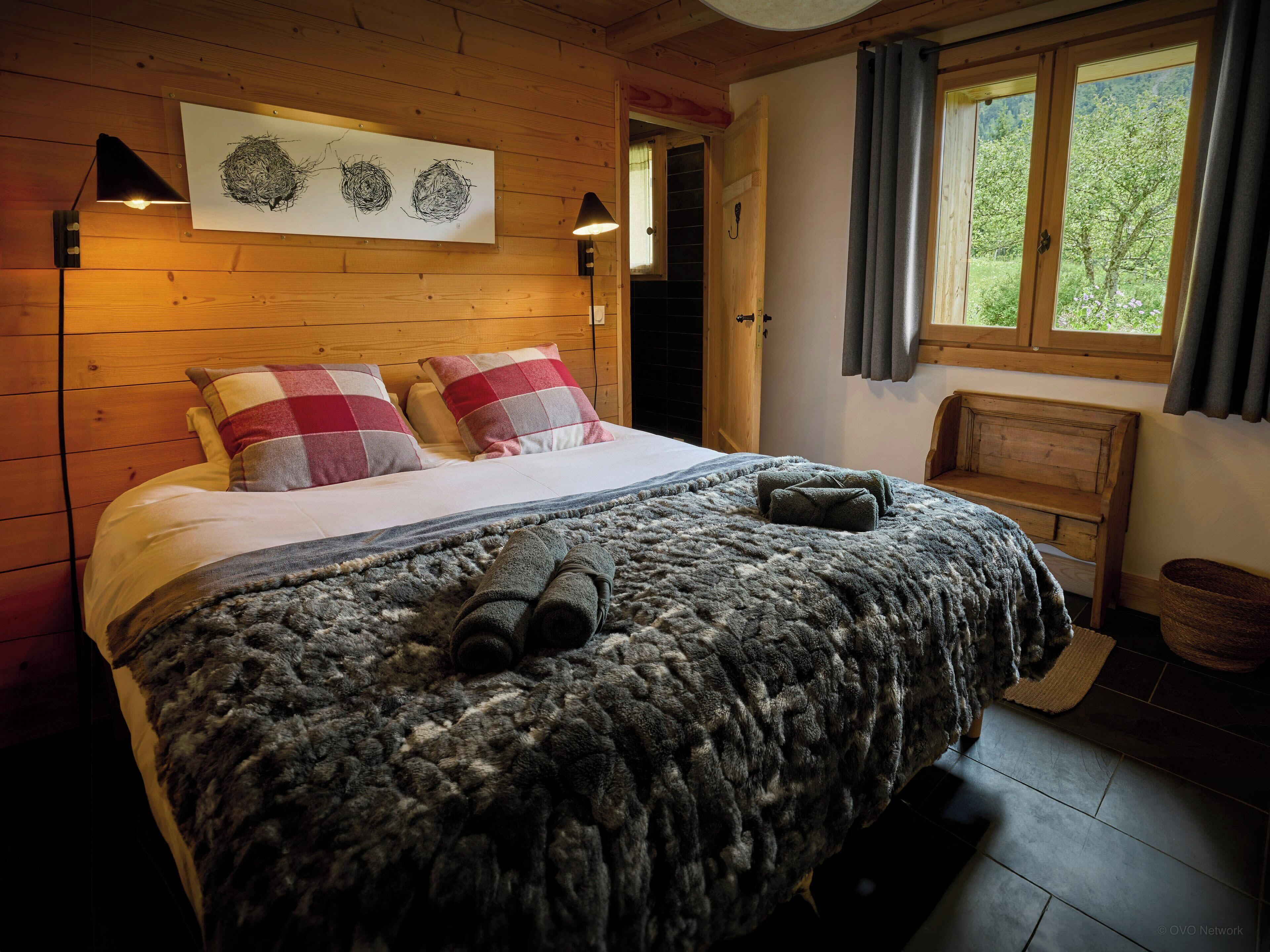 A cozy wooden room with a bed, a bench, and a window with curtains.