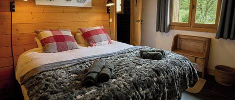 A cozy wooden room with a bed, a bench, and a window with curtains.