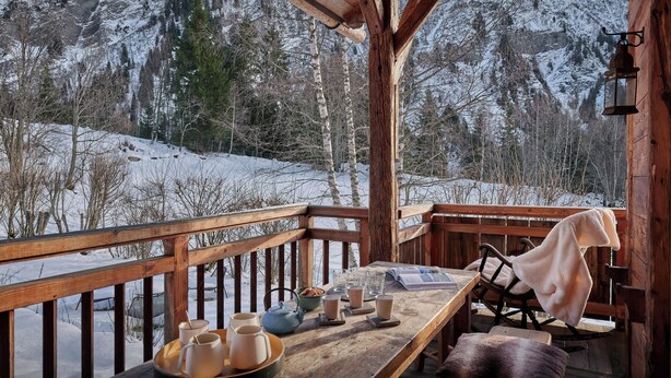 A wooden deck with a table set for dining, overlooking a snowy mountain landscape.
