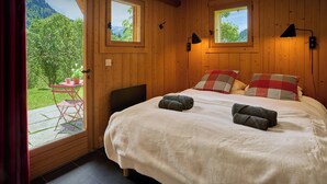 A wooden room with a bed, two windows, and a view of greenery outside.