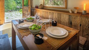 Ein Holztisch ist mit Tellern, Schüsseln und Gläsern gedeckt, mit Blick auf einen Garten und Berge durch ein offenes Fenster.