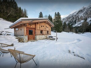 A wooden cabin with a stone foundation, a wooden door, and a window with heart-shaped cutouts.