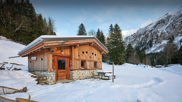 Eine Holzhütte mit Steinunterbau, einer Holztür und einem Fenster.