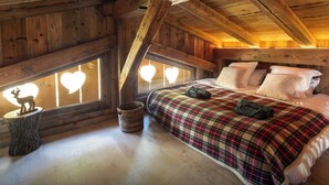 Ein gemütliches Schlafzimmer unter dem Dach mit Holzbalkendecke, einer karierten Bettdecke und einer Hirschdekoration auf der Fensterbank.