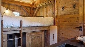 Una habitación rústica de madera con una litera, un armario pequeño, una puerta decorada con cuernos de ciervo y un reloj.
