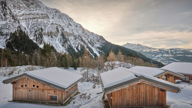 Cabañas de madera con tejados nevados en una zona montañosa.