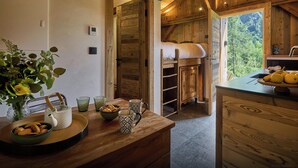 Una cocina rústica con vigas de madera, un mostrador de madera con un frutero, y vistas al bosque a través de una ventana.