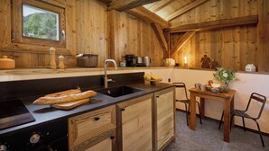 Cocina de cabaña de madera con encimera negra, armarios de madera, un lavabo y ventana con vistas a un bosque.