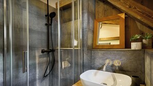 Un baño moderno con cabina de ducha de vidrio, un estante de madera con plantas y un lavamanos grande y blanco.