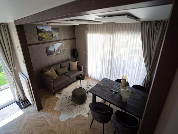 A modern living room with a sofa, a dining table, and a large window with curtains. - Comfortable Chalet Near the Pressegger See (Hermagor-Pressegger See)