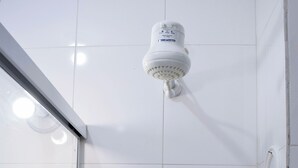 Un baño con azulejos blancos, un cabezal de ducha, una puerta de cristal para la ducha, un lavamanos y un perchero para toallas.
