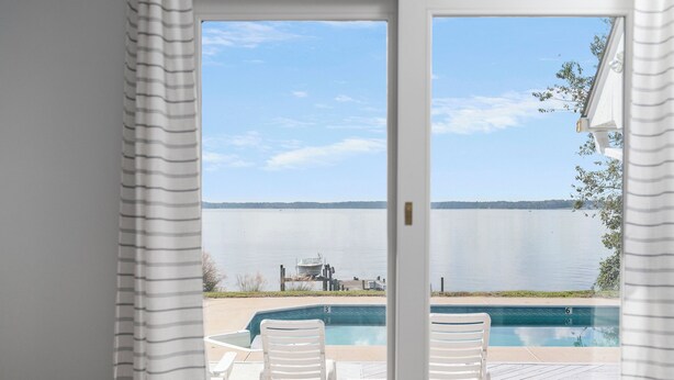 A view from a room with a sliding glass door to a pool area, featuring a clear view of a lake and a dock with a boat.